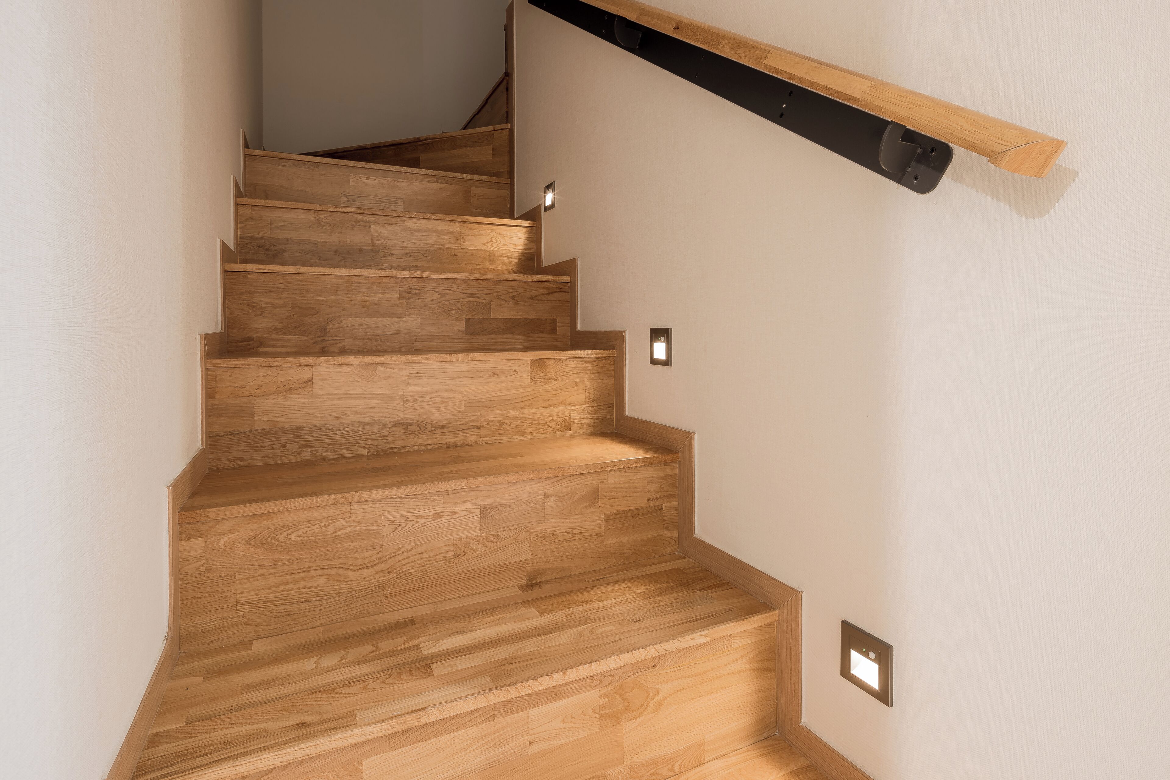 A wooden staircase with a handrail and wall-mounted light switches.