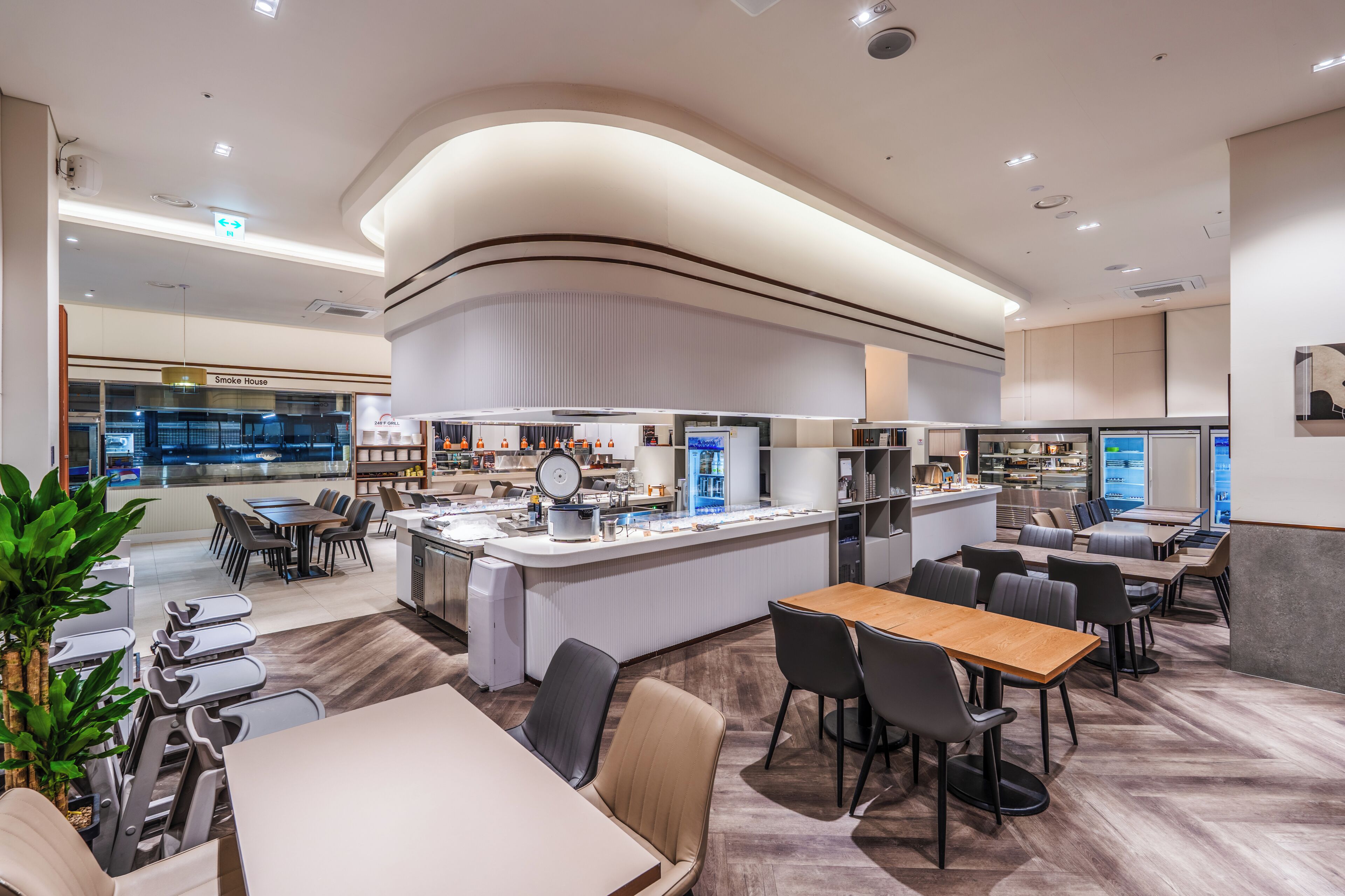 A modern restaurant with a central bar, multiple dining areas, and a visible kitchen area.