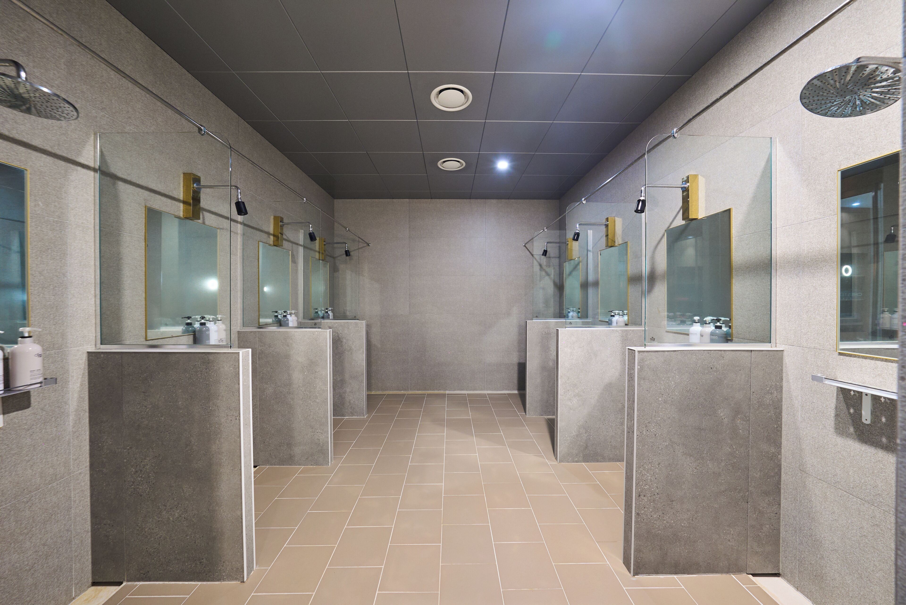 A modern bathroom with glass partitions, mirrors, and a tiled floor.