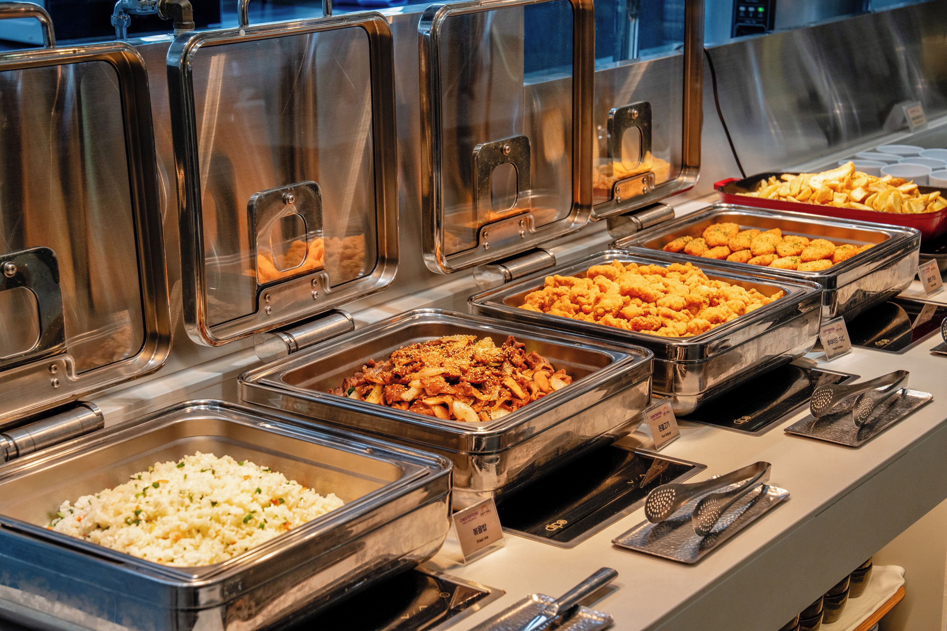 A buffet with various food options in metal containers, utensils, and a sign indicating a price of $8.99.