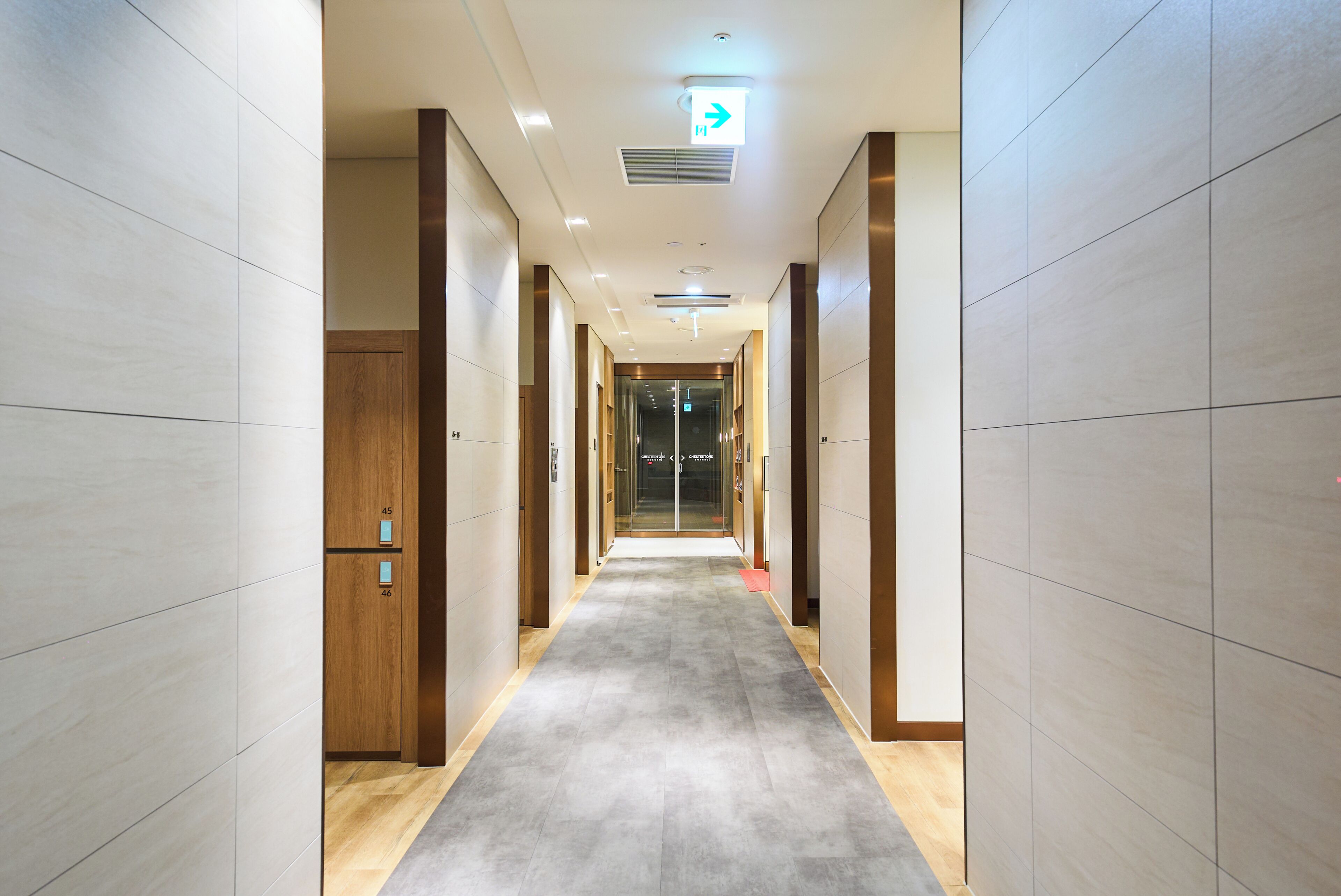 A corridor with a carpeted floor, wooden doors, and a ceiling light.