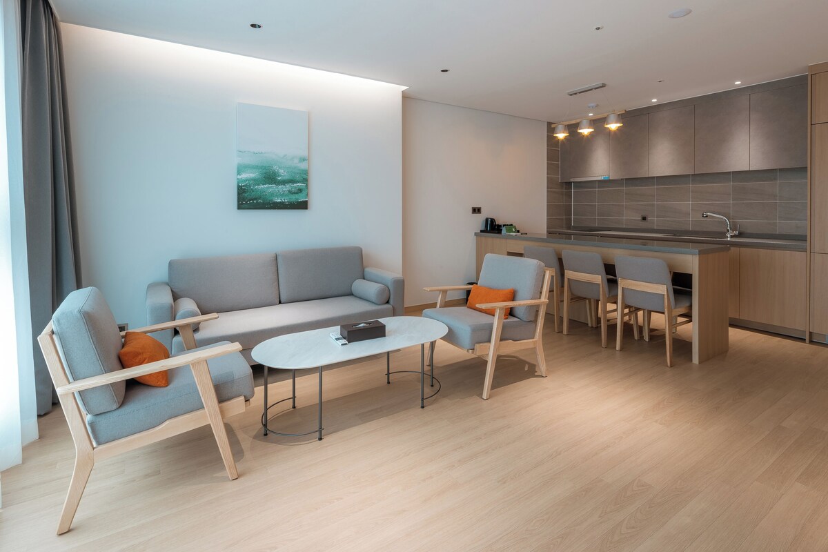 Una sala de estar moderna con sofá, sillas, una mesita de centro y una zona de cocina con una mesa de comedor y sillas.