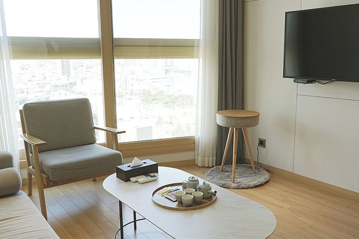 Una sala moderna con un sofá, una mesa de centro con una bandeja, un sillón, una mesita redonda y un televisor montado en la pared.