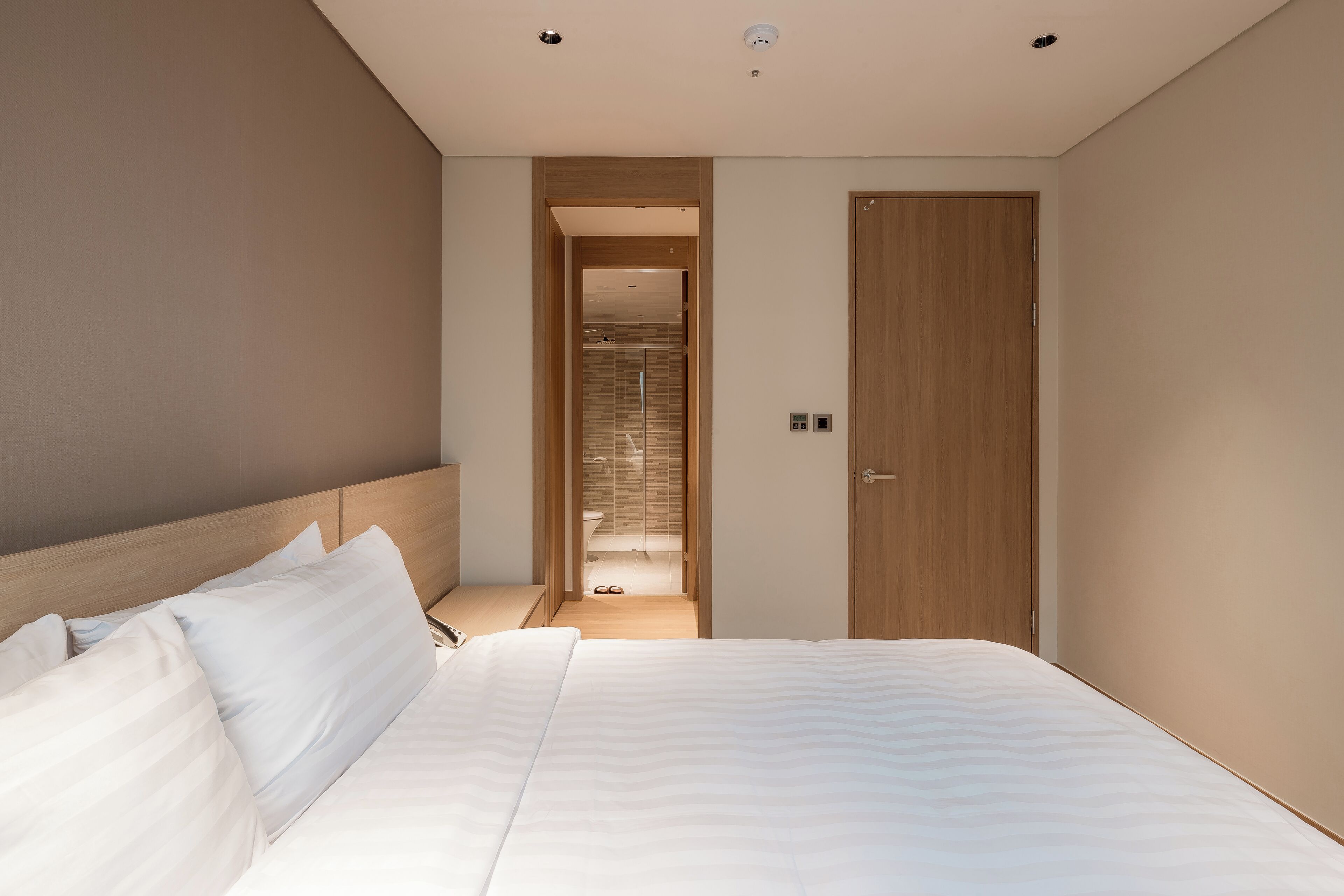 A modern hotel room with a large bed, a wooden wardrobe, and a bathroom visible through an open door.