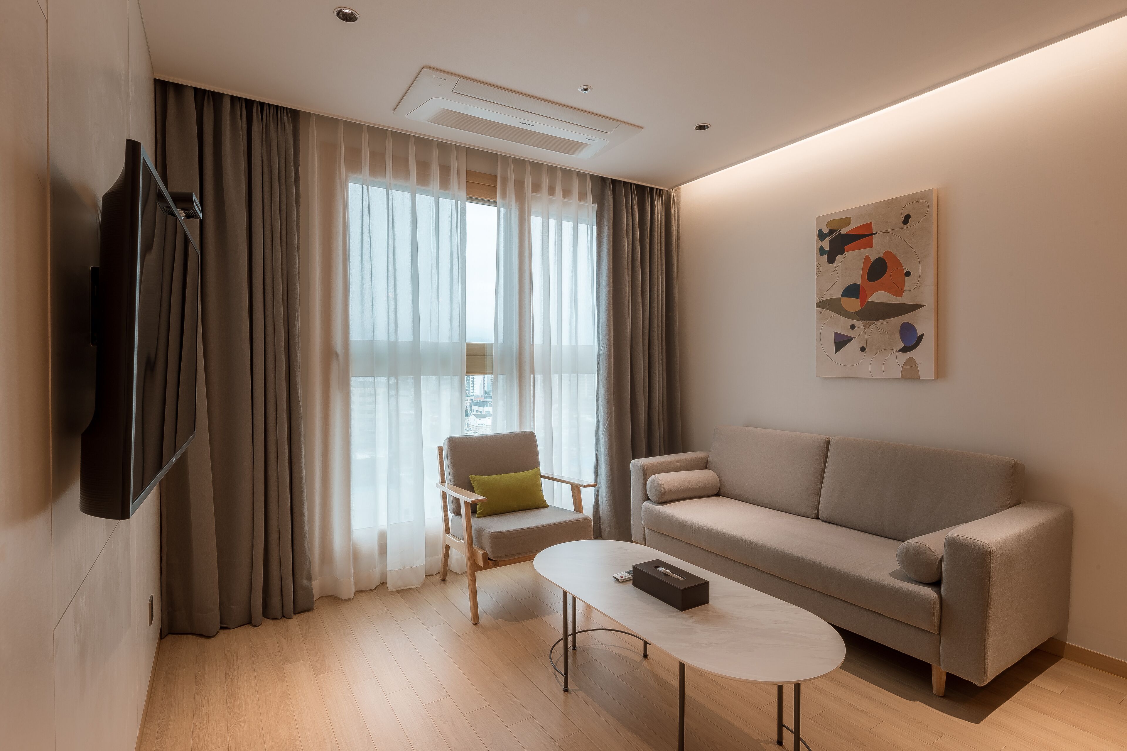 Un salon moderne comprenant un canapé, une table basse, un fauteuil et un téléviseur à écran plat fixé au mur.