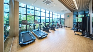 Un gimnasio con cintas de correr, bicicletas estáticas y máquinas de pesas, amplias ventanas y suelo de madera.