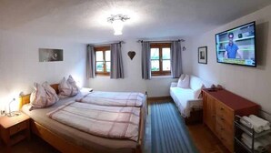 Un dormitorio con dos camas, televisión, cómoda y ventana con cortinas.