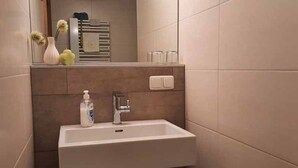 Un baño con un lavamanos blanco, un espejo y un perchero para toallas.