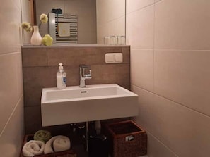 Un baño con un lavamanos blanco, un espejo y un perchero para toallas.