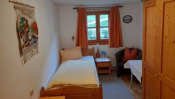 Ein Schlafzimmer mit zwei Betten, einem Schreibtisch, einem Stuhl, einem Kleiderschrank und einem Fenster mit Vorhängen.
