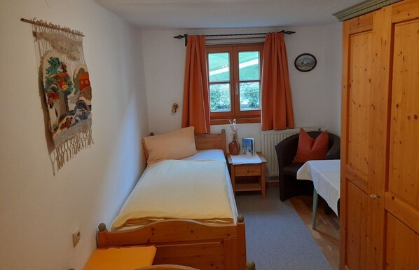 A bedroom with two beds, a desk, a chair, a wardrobe, and a window with curtains.