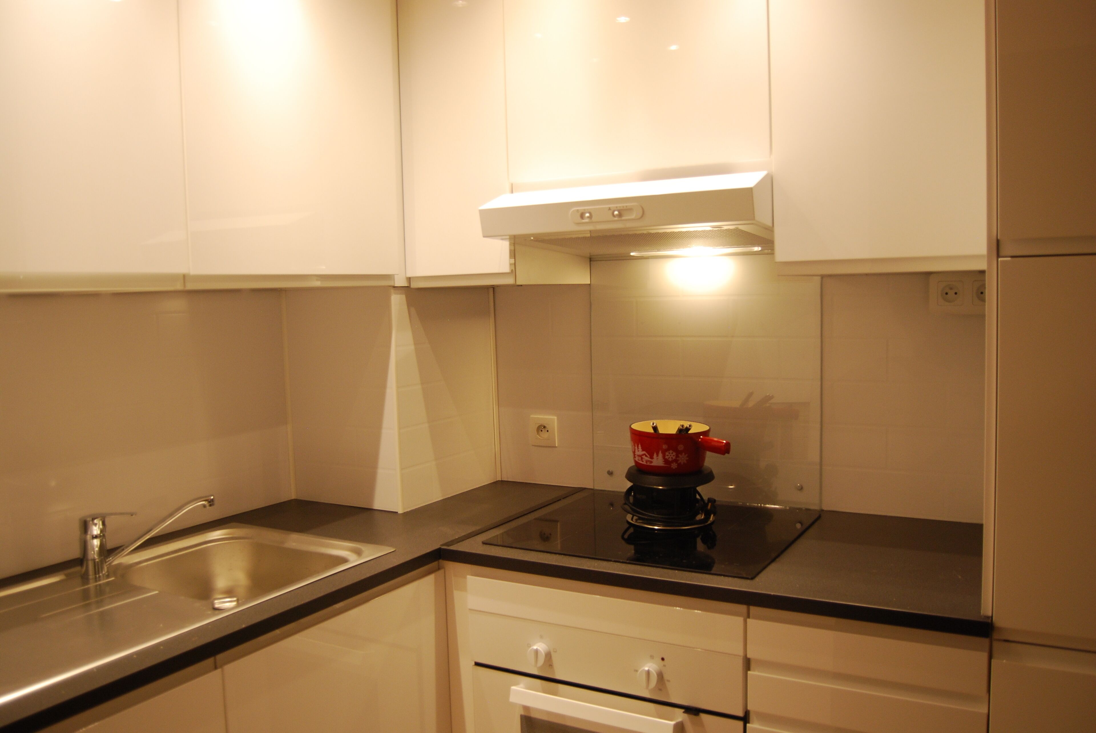 A modern kitchen with a stainless steel sink, a black induction cooktop, and white cabinetry.