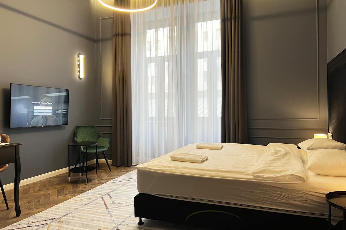 A hotel room with a bed, a TV mounted on the wall, a desk, and a chair.