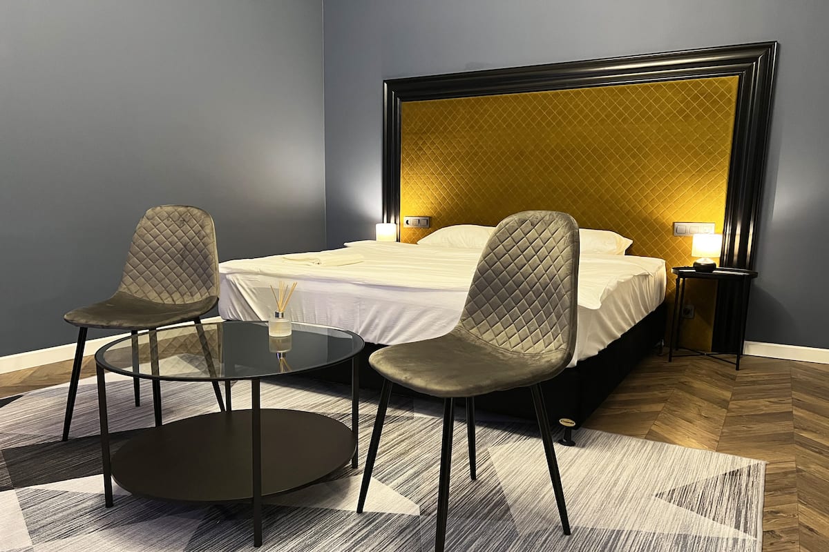 A hotel room with a bed, two chairs, a small table, and a nightstand with a lamp.