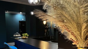 Un espace bar avec des tabourets bleus, un comptoir agrémenté d’un vase contenant des plumes d’herbe des pampas et une table avec une lampe.