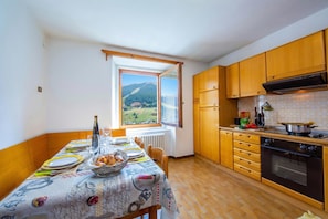 Un comedor con una mesa dispuesta para cuatro, una ventana con vistas a un paisaje montañoso, armarios de madera y un horno empotrado.