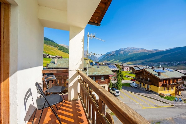 Un balcón con vistas a un paisaje montañoso, baranda de madera y una mesa con sillas.