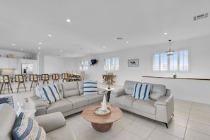 A spacious living area with a large L-shaped sofa, a round coffee table, and a dining area with a kitchen in the background. - Paradise Cove on the Gulf 5 bedroom 3 bath with pool Ice Machince dockage, kayaks, bikes, paddleboards and more (Marathon)