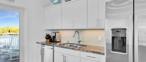 Una cocina moderna con armarios blancos, un refrigerador de acero inoxidable, un dispensador de agua integrado y vistas a un balcón con mobiliario exterior.