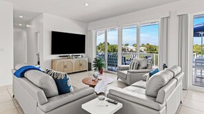 A modern living room with a flat-screen TV, two sofas, a coffee table, and a view of the outdoors.