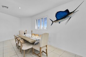 Ein Esszimmer mit großem Tisch, Stühlen, einem Fenster und einer Wanddekoration mit einem Fisch.