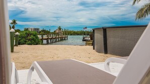 A beach view with a wooden pier, a boat, and a building with an American flag. - 5 Seas Retreat 4 bed 2 bath dock, pool, Sandy Beach Dockage For up to a 25 ft boat (Marathon)