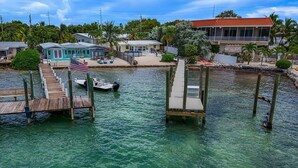 A waterfront property with a dock, a boat, and a house with a red roof. - 5 Seas Retreat 4 bed 2 bath dock, pool, Sandy Beach Dockage For up to a 25 ft boat (Marathon)