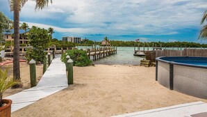 A beachside walkway leading to a dock, a pool, and a building with a view of the water. - 5 Seas Retreat 4 bed 2 bath dock, pool, Sandy Beach Dockage For up to a 25 ft boat (Marathon)