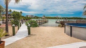 A beachside walkway leading to a dock, a pool, and a building with a view of the water.