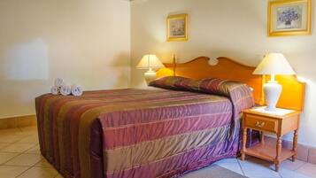 A hotel room with a bed, two bedside lamps, a wooden nightstand, and two framed pictures on the wall.