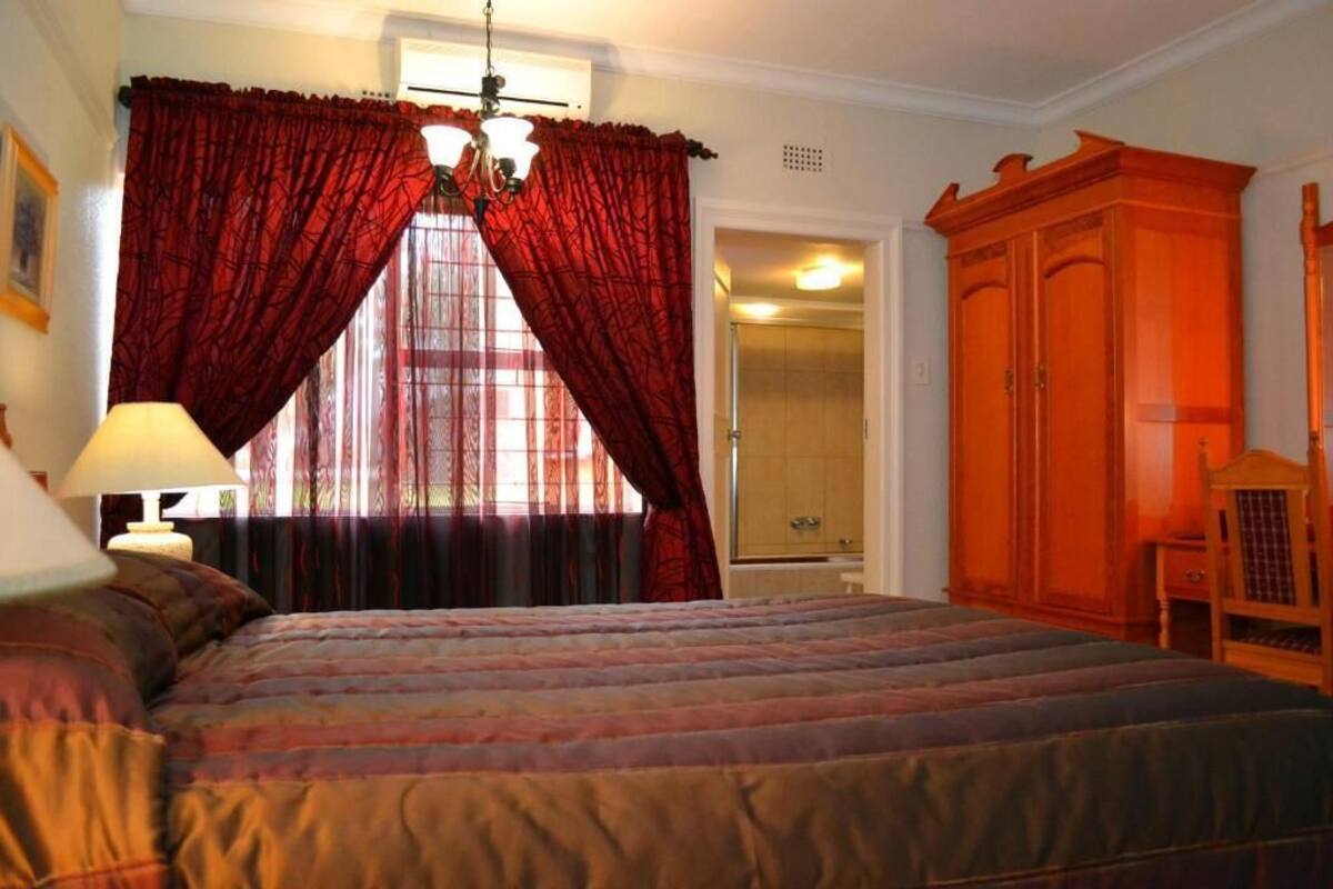 Quarto com uma cama grande, um guarda-roupa de madeira e uma janela com cortinas vermelhas.
