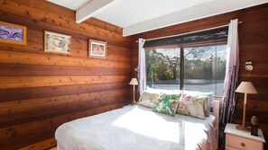 Une chambre à coucher aux murs lambrissés, avec un lit, deux lampes de chevet et trois œuvres d’art encadrées accrochées au mur.