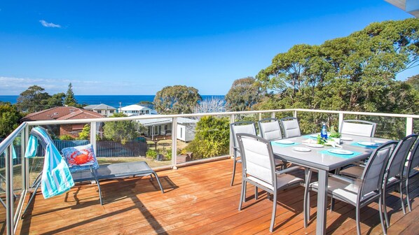 Une terrasse avec une table dressée pour le repas, offrant une vue sur un quartier résidentiel et l’océan.