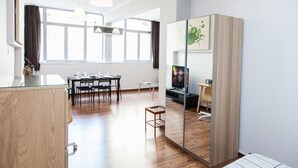 A modern room with a wooden floor, a dining table with chairs, a TV, and a large mirror.