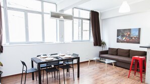 A modern living room with a dining area, large windows, and a painting on the wall.