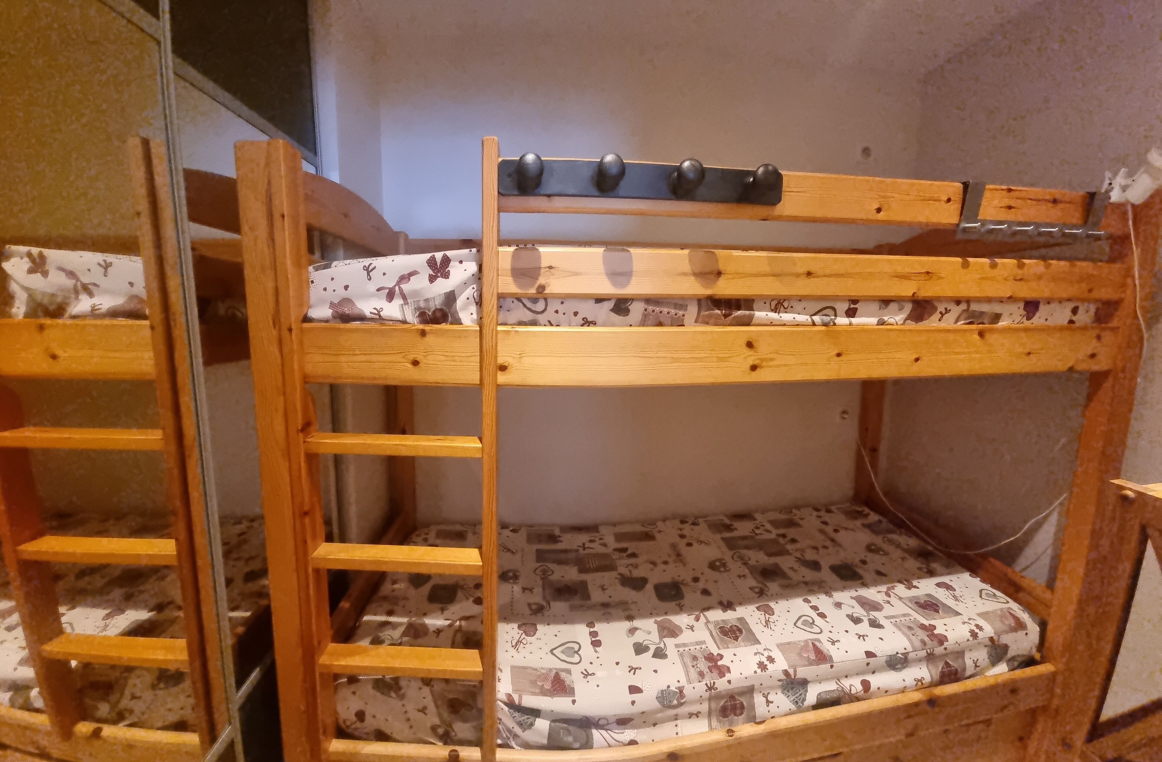 Een stapelbed met een ladder, een gestreept matras en een hoofdbord met haken.