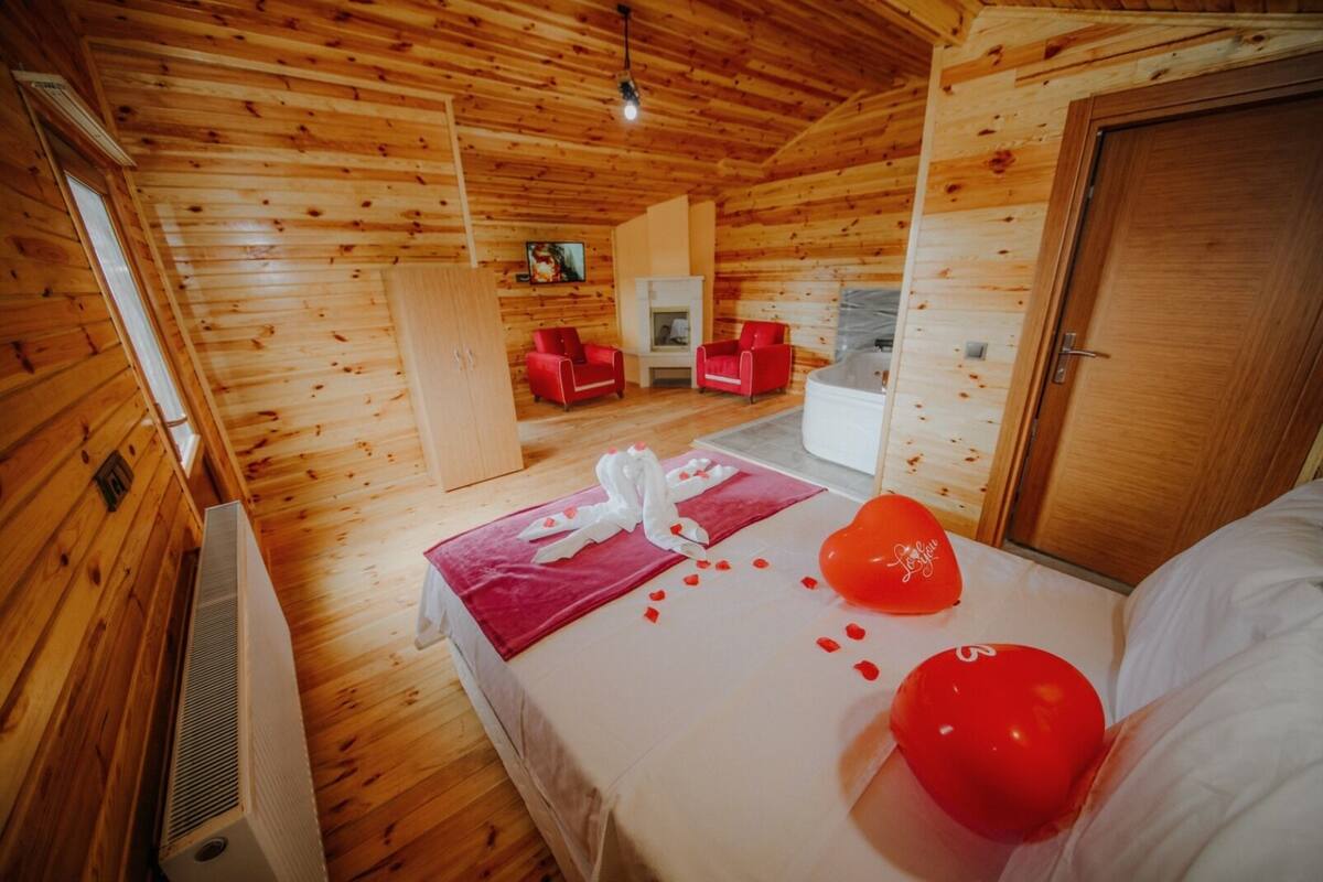 A wooden cabin room with a bed, a red heart-shaped balloon, and a towel on the bed.
