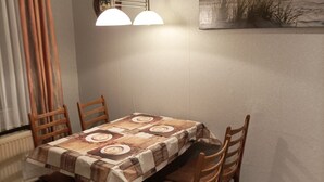 A dining area with a table set for four, wooden chairs, a patterned tablecloth, and a painting of a sunset on the wall. - Vacation apartment (Moormerland)