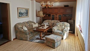 A living room with two sofas, a coffee table, and a chandelier. There is a cabinet with glass doors and a painting on the wall. - Vacation apartment (Moormerland)