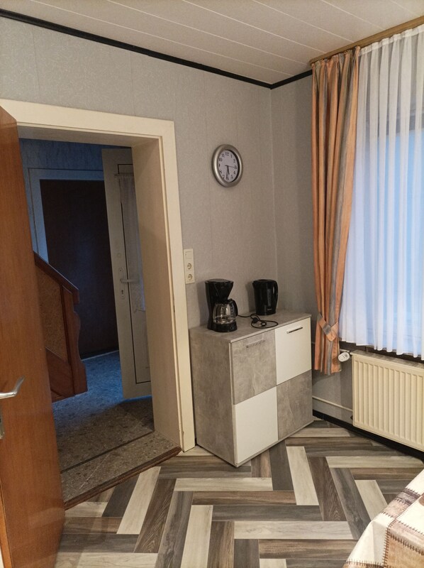 Une petite pièce, de taille modeste, comprenant un coin cuisine, une horloge au mur et une fenêtre avec des rideaux.