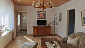 A living room with a wooden ceiling, a chandelier, a television, a cabinet, a sofa, and a coffee table. - Vacation apartment (Moormerland)