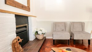 A living room with a fireplace, two grey armchairs, a wooden coffee table with fruit, and a white wall with a wooden frame above the fireplace. - 5 Sea Way (Bognor Regis)