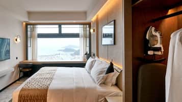 Ein Hotelzimmer mit einem großen Bett, einem Schreibtisch, einem Stuhl, einem Fernseher und Blick auf den Strand.