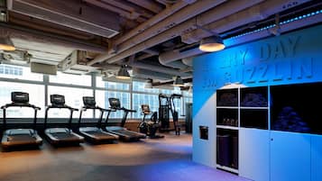 Ein Fitnessraum mit Laufbändern, einem an der Wand befestigten Trainingsgerät und einer Wand mit dem Schriftzug 'EVERY DAY MUGZLIN'.