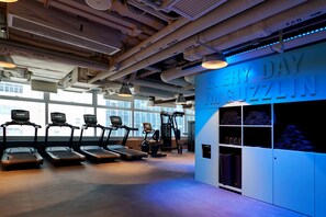 A gym with treadmills, a wall-mounted exercise machine, and a wall with the text 'EVERY DAY MUGZLIN'.