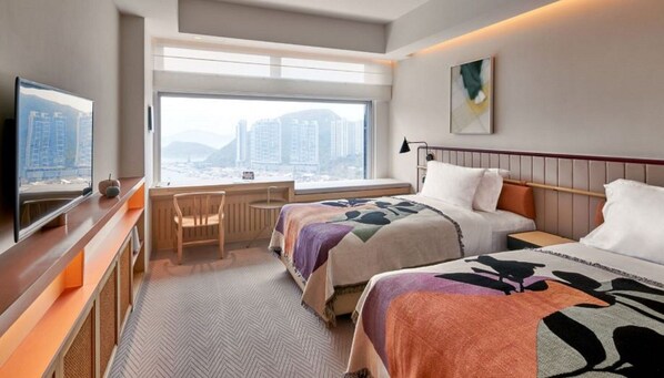 A hotel room with a bed, a desk, a chair, a TV, and a large window with a city view.