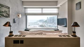 Een moderne slaapkamer met een groot raam, een bed, bedlampjes en een flatscreen televisie.