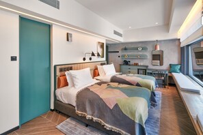 A modern hotel room with two beds, a small desk, a seating area by the window, and a kitchenette. - The Arca (Hong Kong Island)