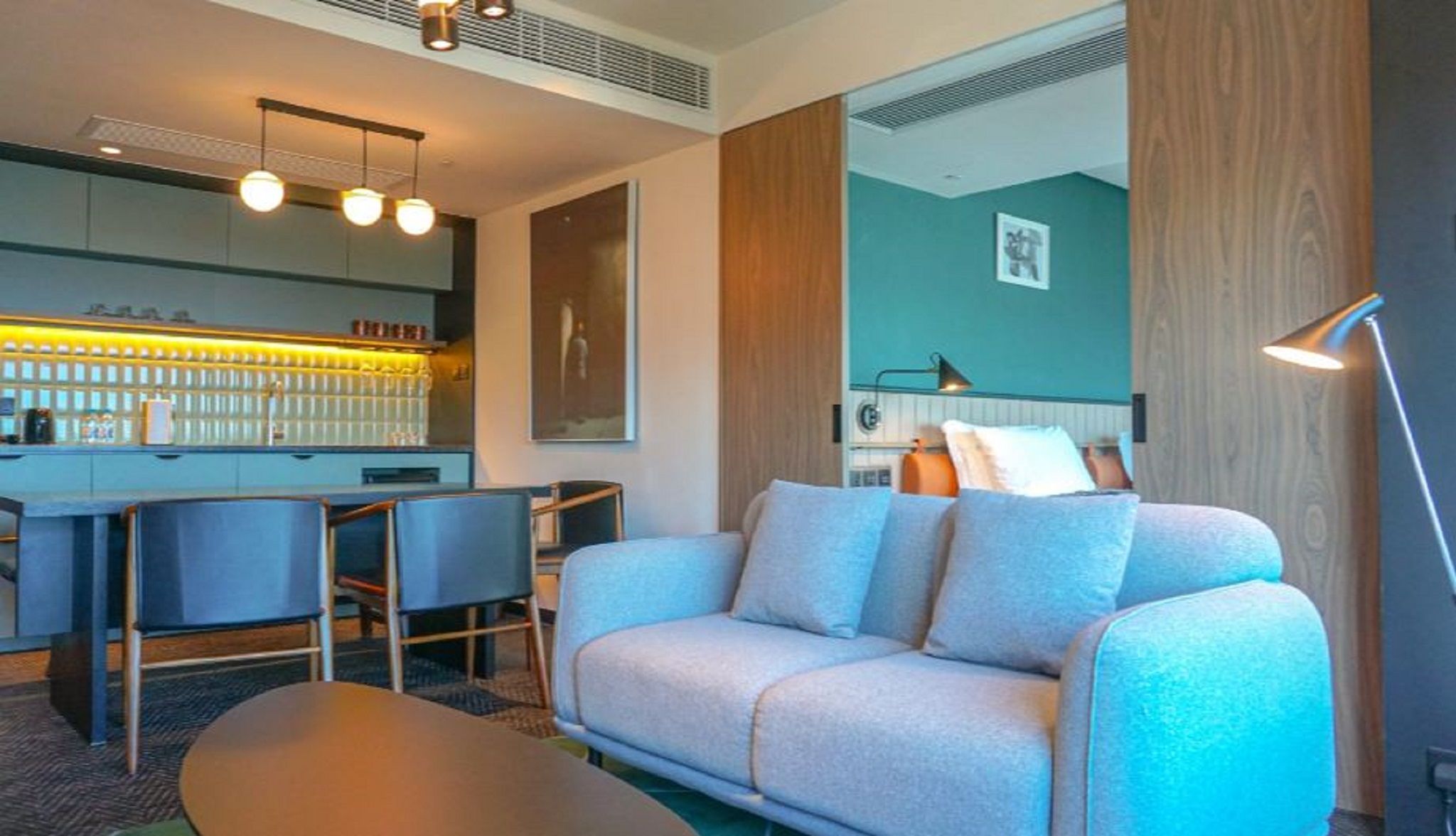 Una sala de estar moderna con un sofá, sillas, una mesa de centro, un área de bar y una lámpara.