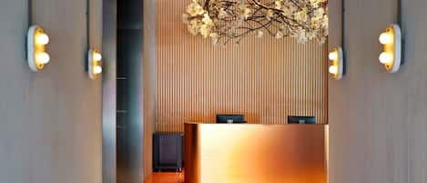 Un mostrador de recepción de diseño moderno, una lámpara colgante decorativa y un panel de pared de madera vertical.